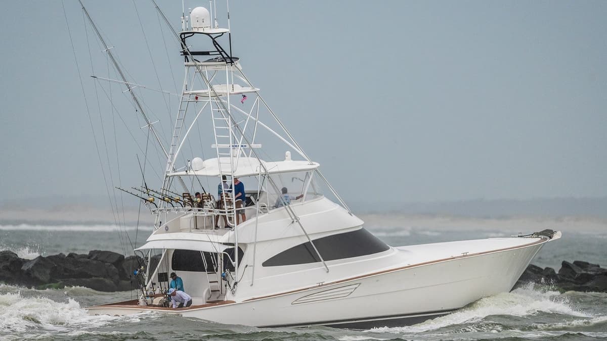 A sportfishing yacht with a sleek white design navigates through choppy waters, equipped with multiple fishing rods