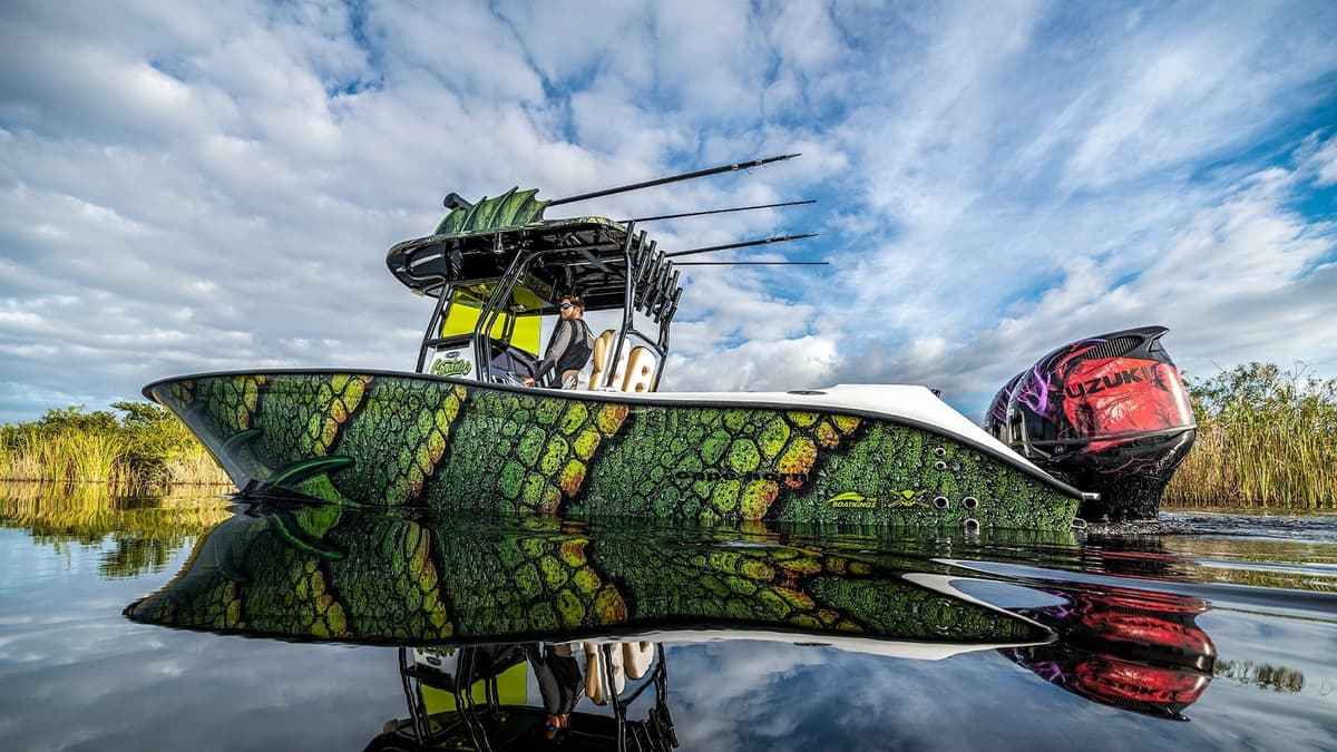 Sportfishing boat with unique green and yellow reptile-patterned hull, equipped with fishing rods, on calm waters