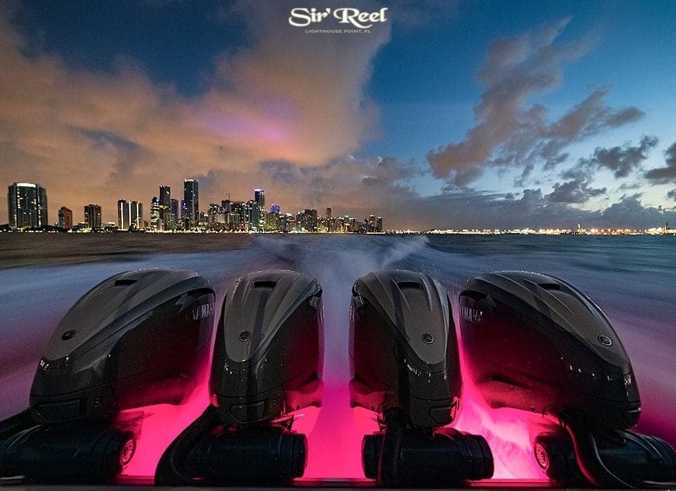 Sportfishing boat with four powerful outboard engines illuminated by pink lights, cruising with a vibrant city skyline