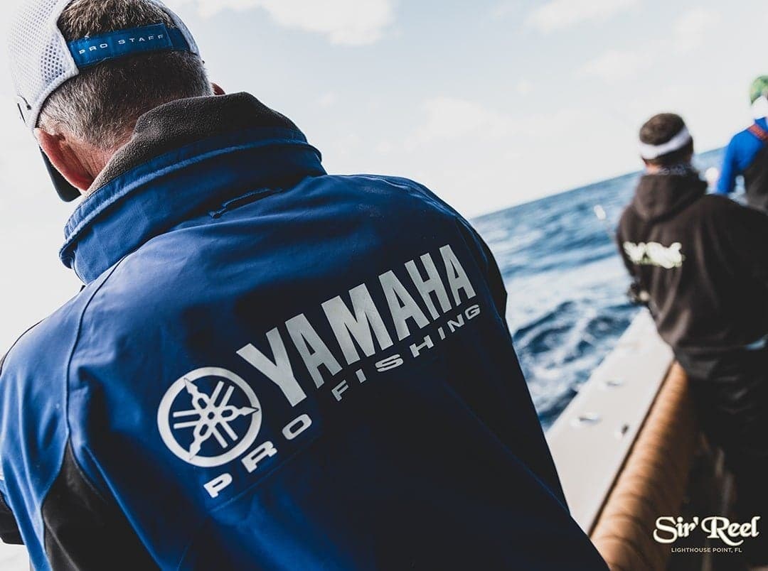 Anglers on a boat engaged in sportfishing, wearing Yamaha Pro Fishing jackets with a vast ocean backdrop