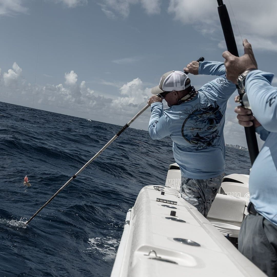 Two anglers in blue shirts engaged in sportfishing on a boat in choppy seas