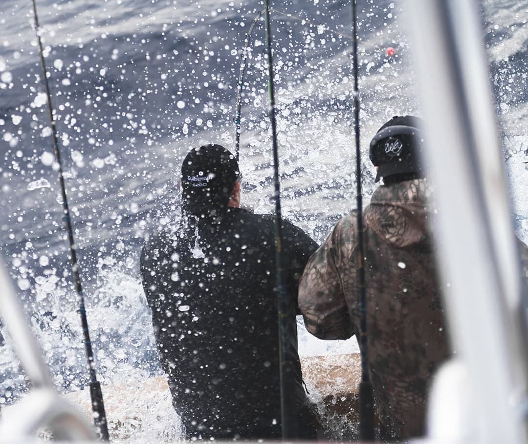 Two anglers on a sportfishing boat captured from behind as they face ocean spray while deep sea fishing