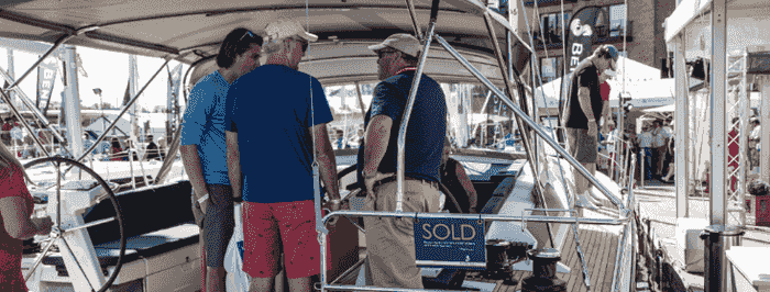 Boat broker and client standing on a yacht marked as sold at a marina